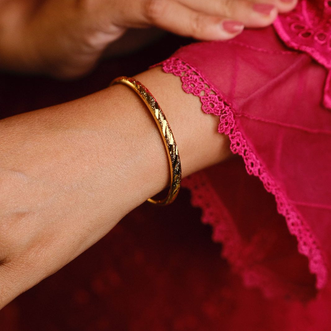 Close-up of a person's wrist with a gold bracelet on a red fabric background
